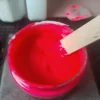 Nahaufnahme von geöffneter Dose mit Neon-Pinker Textildruckfarbe. In der farbe steckt ein Holzmundpatel, mit dem die Farbe aufgerührt wurde.