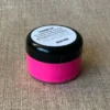 Kleine, runde und durchsichtige Dose mit schwarzem Declek gefüllt mit pinker Textildruckfarbe. Ein weißer Inhalts-Aufkleber klebt auf dem Deckel.