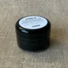 Kleine, runde und durchsichtige Dose mit schwarzem Declek gefüllt mit schwarzer Textildruckfarbe. Ein weißer Inhalts-Aufkleber klebt auf dem Deckel.