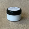 Kleine, runde und durchsichtige Dose mit schwarzem Declek gefüllt mit weißer Textildruckfarbe. Ein weißer Inhalts-Aufkleber klebt auf dem Deckel.